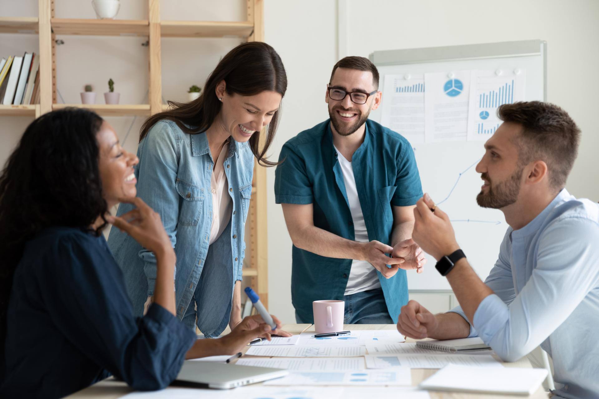 Smiling diverse colleagues gather in boardroom brainstorm discuss financial statistics together